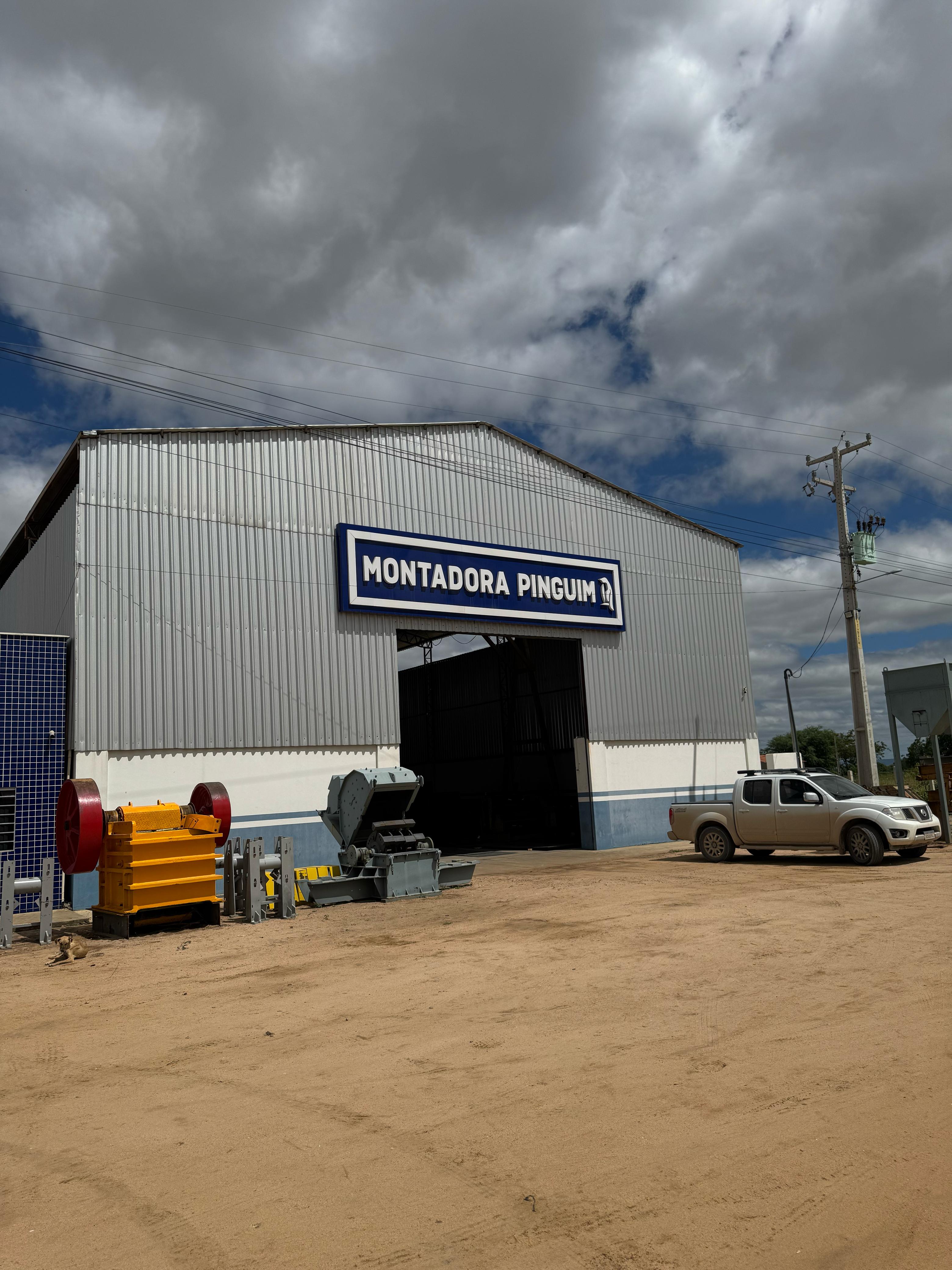 Fábrica da Montadora Pinguim com galpão industrial, equipamentos de britagem e placa de identificação
